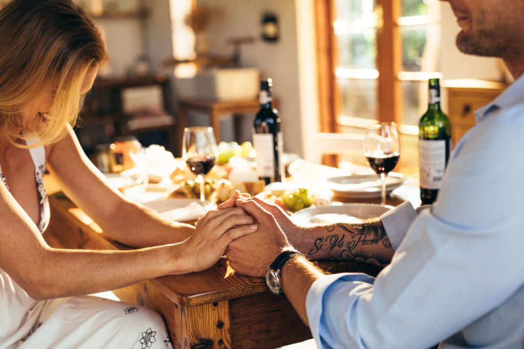 Ein Paar sitzt bei einem romantisch gedeckten Tisch, hält sich an den Händen und genießt ein privates Dinner in gemütlicher Atmosphäre – zubereitet von einem Mietkoch für Zuhause.