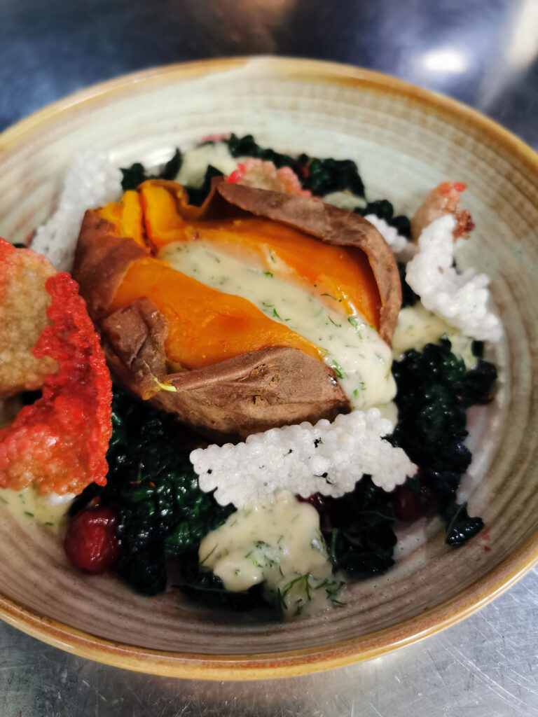 Kreativ angerichtetes vegetarisches Gericht mit gebackener Süßkartoffel und cremiger Kräutersauce