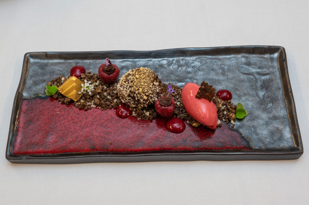 Kreativ angerichtetes Dessert mit Schokoladenkugel und frischen Himbeeren